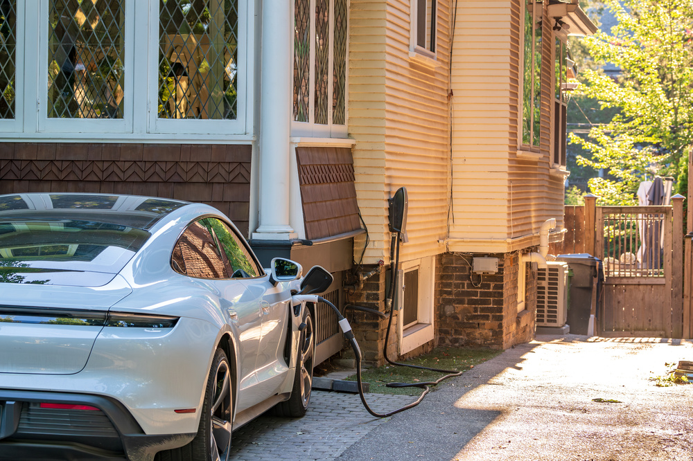 Gros plan d’un véhicule électrique à haut rendement relié à une station de recharge dans une entrée résidentielle.