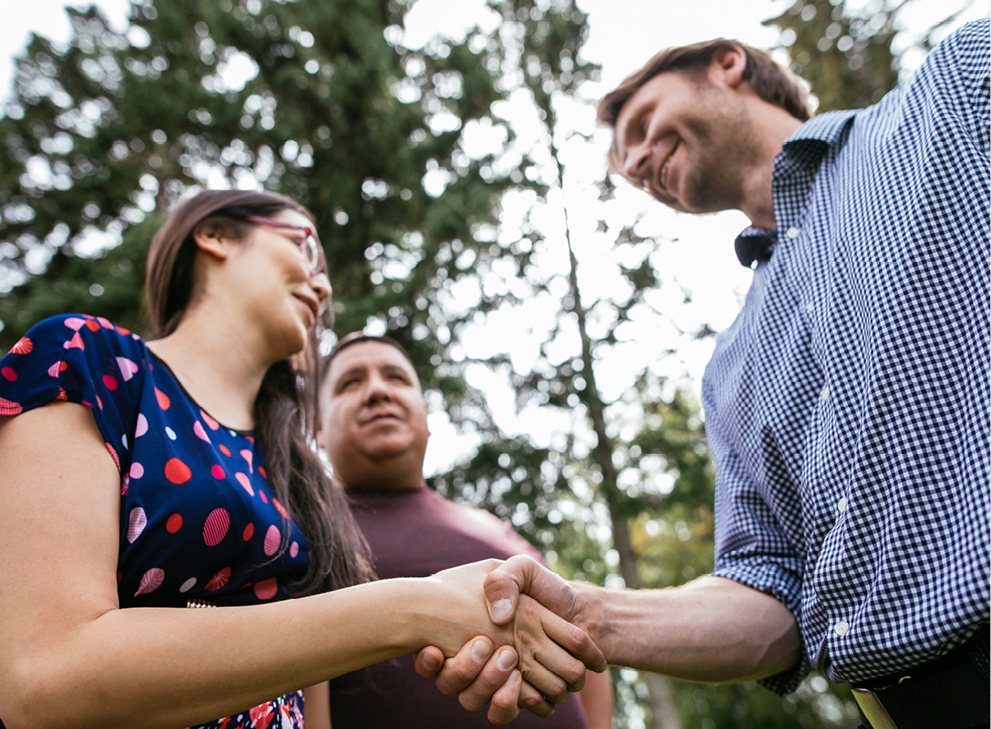 A man and a woman shaking hands while a third man looks on.