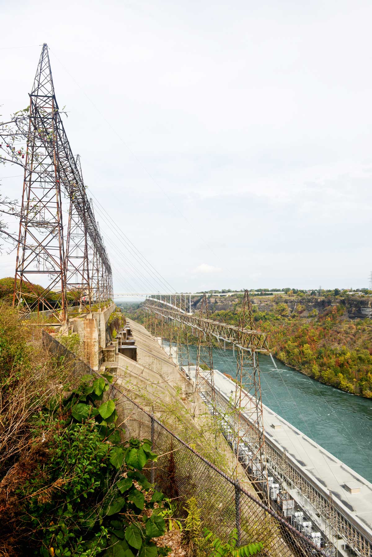Side view in summer of the Sir Adam Beck hydroelectric station with transmission lines above the station, and the Niagara river below.